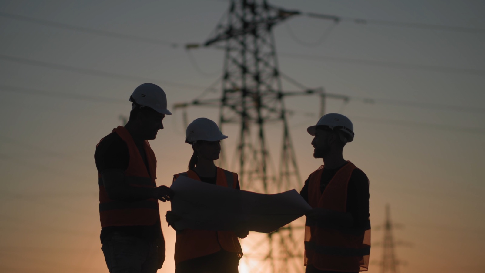 Engineers reviewing infrastructure plans near power transmission towers at dusk